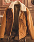 Tan corduroy barn jacket with cream sherpa collar and lining, hung open over a wooden chair