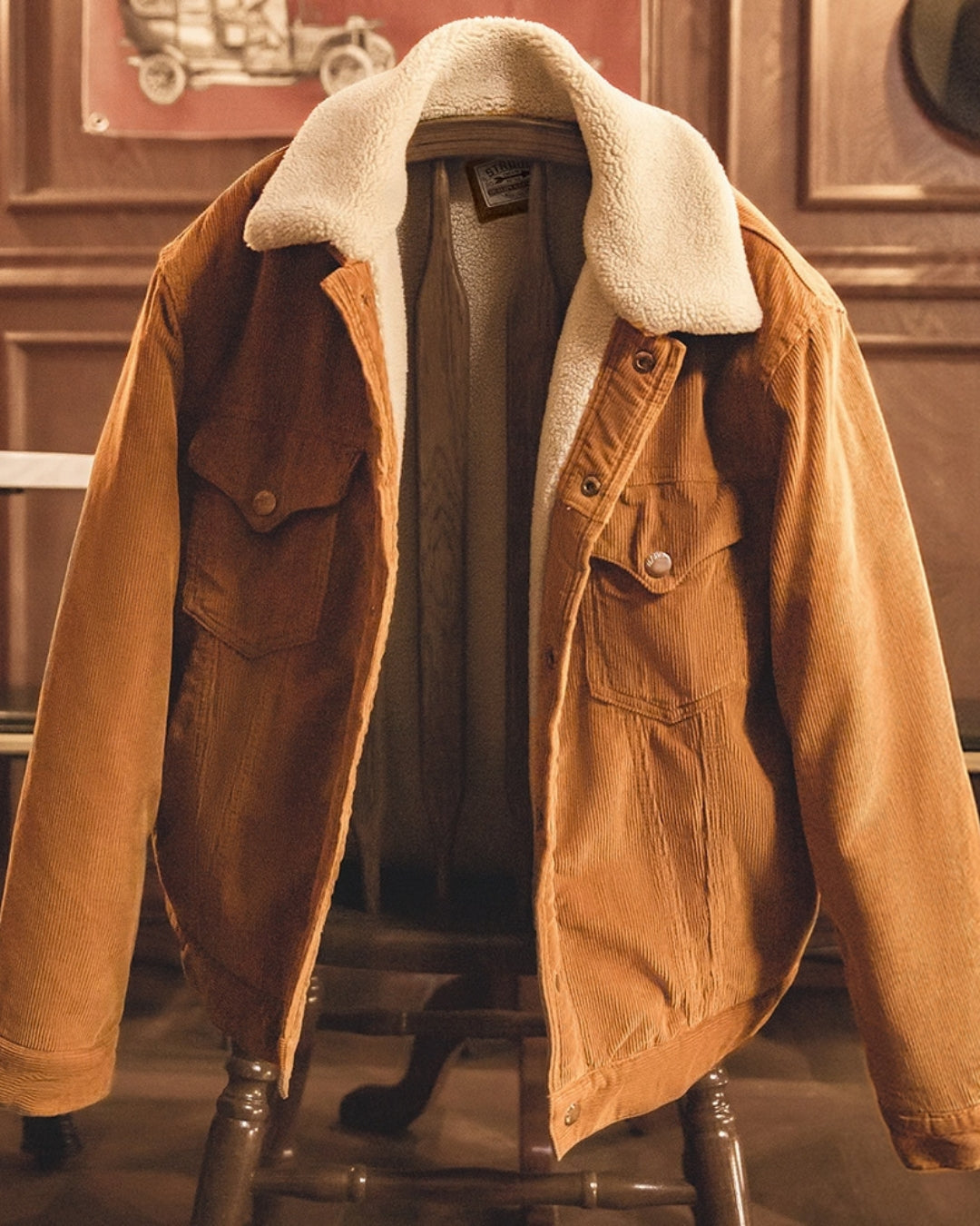 Tan corduroy barn jacket with cream sherpa collar and lining, hung open over a wooden chair